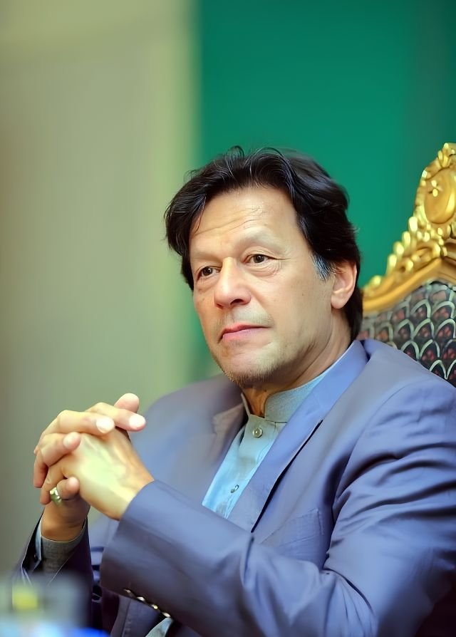 Close-up portrait of Imran Khan with clasped hands sitting in the Prime Minister's Office in Islamabad wearing a blue suit jacket.