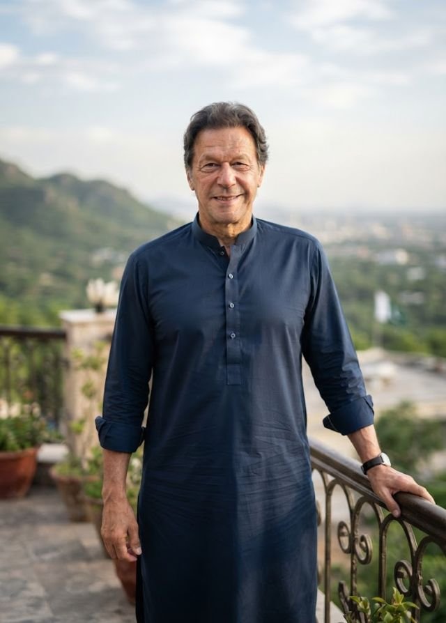 Imran Khan smiling portrait wearing a navy blue shalwar kameez outdoors against a scenic mountain backdrop.